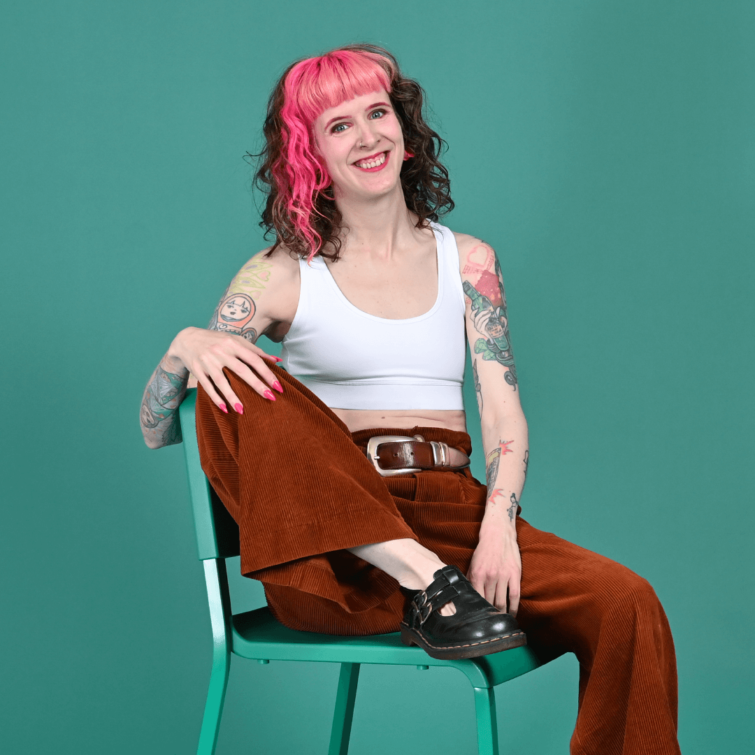 Tracy is wearing a white racerback bralette and trousers sitting on a chair